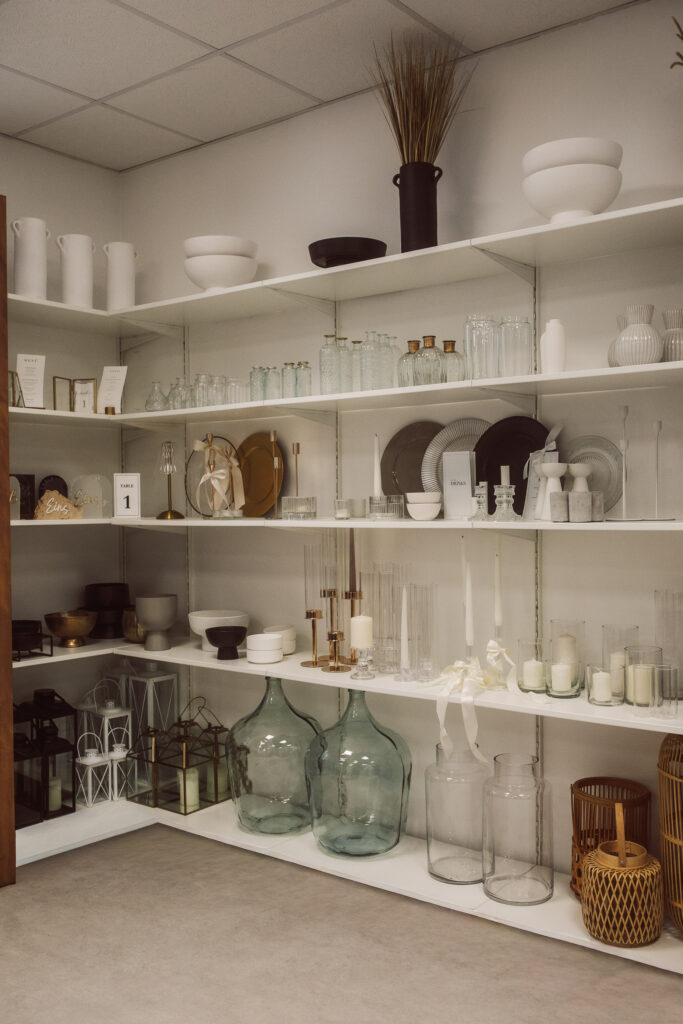 Regale mit Glasvasen, Gläsern, Schalen, Kerzen, Windlichtern und verschiedenen Dekorationsartikeln in einem gut beleuchteten, organisierten Raum mit einer neutralen Farbpalette - die perfekte Inspiration für Event & Floral Design Hochzeit oder hochzeitsfloristik in Niederbayern.