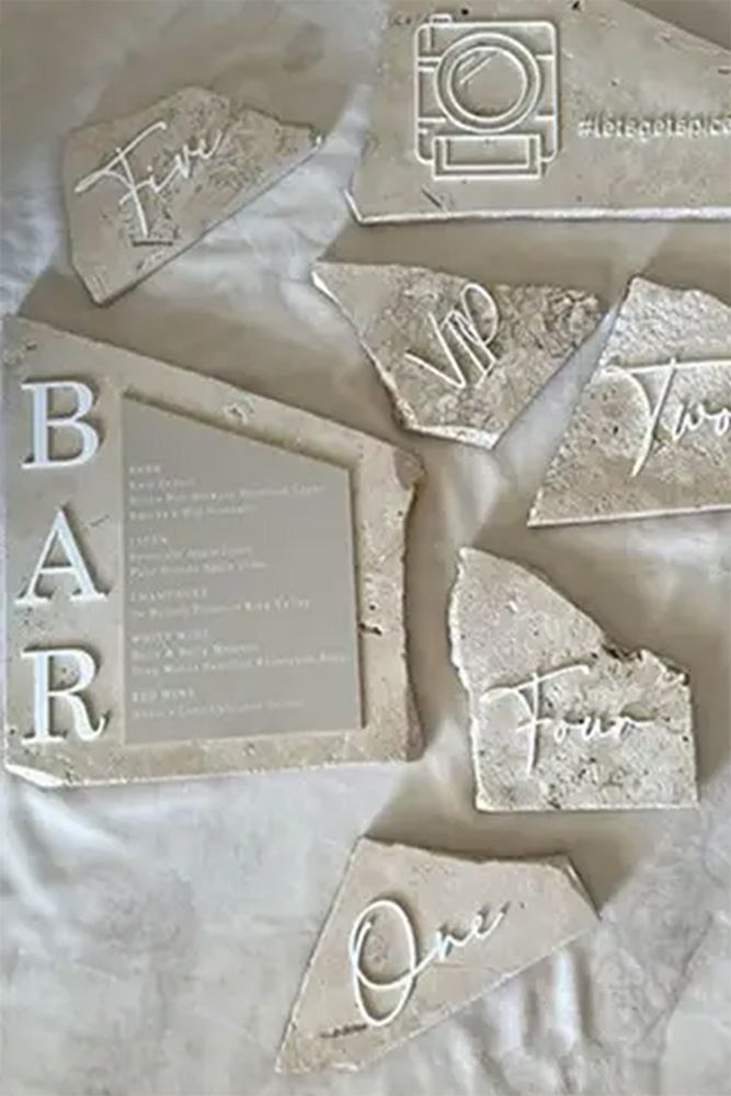 Gebrochene Steinstücke mit eingravierten Worten von Dominique Kubicek: "BAR" auf einem großen Stück mit einer Getränkekarte, und die Zahlen Eins, Zwei, Vier, Fünf und VIP auf kleineren Stücken - perfekte Akzente für mondhaende oder hochzeitsfloristische Displays.